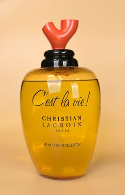 un flacon de parfum jaune avec un bouchon rouge sur fond beige