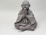 figurine de Bouddha assis sur une surface blanche, les mains devant la bouche