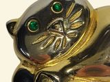 a gold cat brooch with green eyes laying on the ground