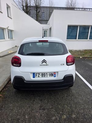 une voiture blanche garée dans un parking à côté d'un bâtiment
