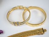 two gold bracelets and a bracelet with a purple stone