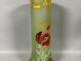 a green vase with red flowers on it on a table