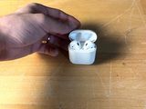 une personne tenant des AirPods d'Apple posés sur une table en bois