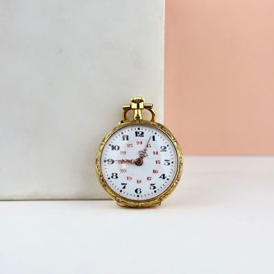 une petite montre en or posée sur une table blanche