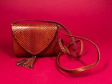 a brown purse with a tassel on a pink background