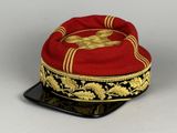 un chapeau rouge orné de broderies dorées, posé sur une assiette noire
