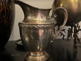 a silver pitcher sitting on top of a table next to a vase