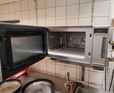un micro-ondes à porte ouverte dans une cuisine où se trouvent des casseroles et des poêles