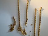 three gold necklaces and two bracelets on a white surface