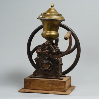 un moulin à café ancien monté sur un socle en bois et muni d'une poignée en métal