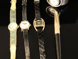 four different watches and a pen are sitting on a black surface