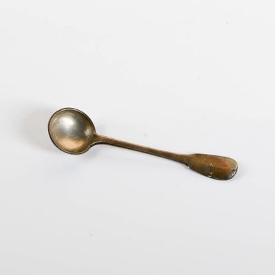 an antique spoon on a white surface with a small spoon sticking out of it