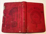 an old red book sitting on top of a table next to a clock