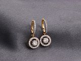 a pair of gold and diamond earrings on a gray cloth