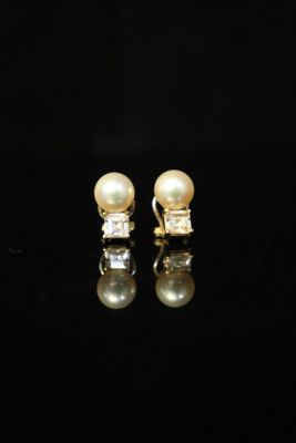 a pair of pearl and diamond earrings on a black surface
