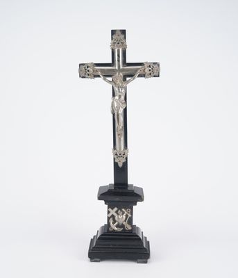 a silver cross on a black pedestal with a white background
