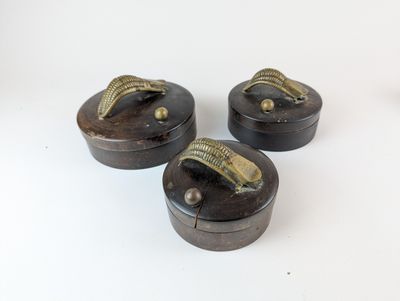 trois petites boîtes en bois munies de poignées métalliques, posées sur une surface blanche