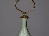 a green vase with a gold handle sitting on top of a table