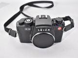 a black camera with a black strap on a white surface