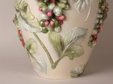 a white vase with a bunch of green and red berries on it