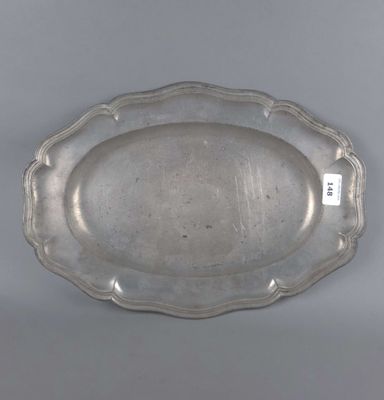 une assiette en argent aux bords festonnés, posée sur un fond gris