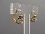 pair of gold and diamond earrings on display on clear acrylic stand