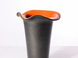 a black vase with an orange handle sitting on a white surface