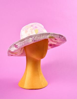 un chapeau rose et blanc posé sur une tête de mannequin, sur fond rose