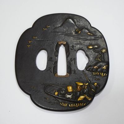 une tsuba en fer ornée de motifs dorés sur fond blanc