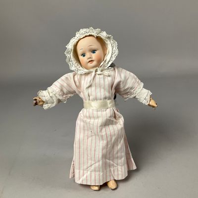 Une poupée à l'ancienne, coiffée d'un bonnet et vêtue d'une robe, est posée sur une surface grise.