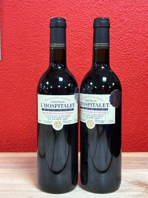 two bottles of wine sitting on top of a wooden table next to a red wall