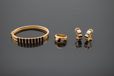 two gold rings and a pair of earrings on a reflective surface
