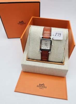 une boîte orange contenant une montre, posée sur une surface blanche
