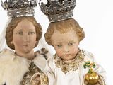 two figurines of two people dressed in white and gold holding a dog