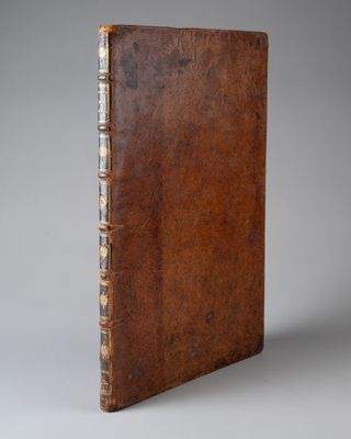 un vieux livre avec une couverture en cuir marron sur fond gris