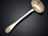 une cuillère ancienne en argent dont le manche repose sur une surface noire