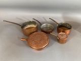 five copper pots and pans sitting on a white surface