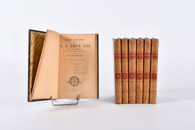 Plusieurs livres anciens sont empilés sur un présentoir devant un fond blanc.