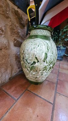 un vase vert muni d'une anse, posé sur un sol carrelé