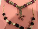 purple and black beaded necklace and bracelet set on a pink background
