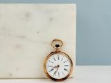 un bloc de marbre blanc sur lequel repose une montre de poche en or