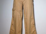 Le pantalon est de couleur beige et comporte des boutons ; il est présenté sur un mannequin.