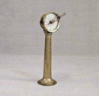 une horloge ancienne en laiton posée sur un socle, sur fond blanc