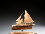 maquette en bois d'un voilier posée sur un socle, sur une surface blanche