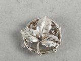 a close up of a silver brooch with a leaf on it