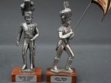 two silver figurines of soldiers holding a flag and a flag