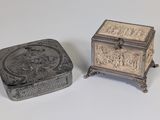 une paire de boîtes en argent ornées de sculptures, posées sur une surface blanche