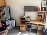 a room with a desk, shelves, and a refrigerator in it