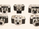 six old cameras are lined up in a row on a white surface