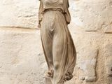 une statue représentant une femme, debout près d'un mur de pierre